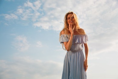 Beautiful young woman against blue sky on sunny day, space for text