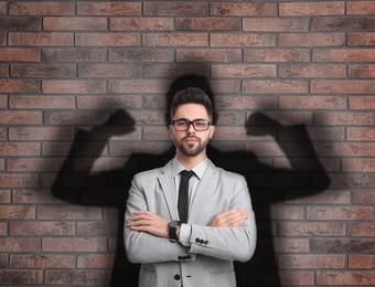 Image of Businessman and shadow of strong muscular man behind him on brick wall. Concept of inner strength