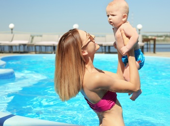 Happy mother with little baby in swimming pool on sunny day