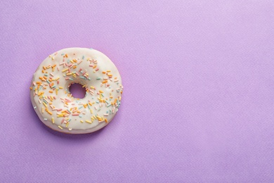 Delicious glazed doughnut with sprinkles on color background, top view