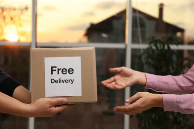 Photo of Woman receiving parcel with sticker Free Delivery from courier indoors, closeup