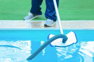 Photo of Male worker cleaning outdoor pool with underwater vacuum