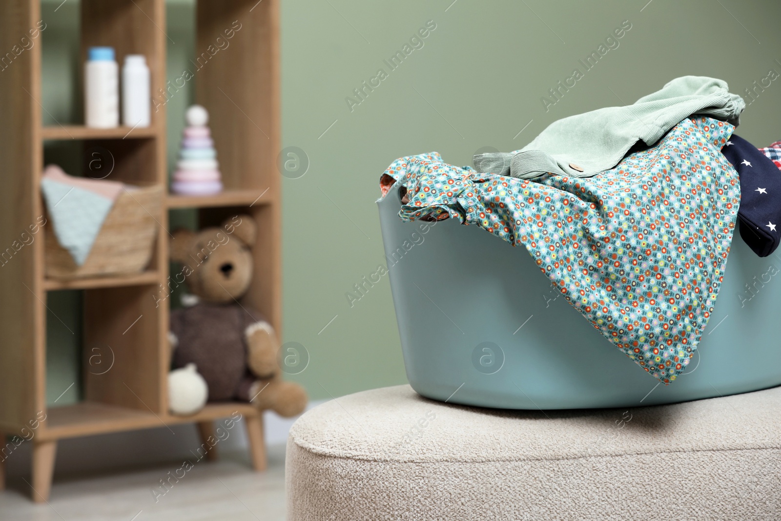 Photo of Laundry basket with baby clothes on light ottoman in child room, space for text