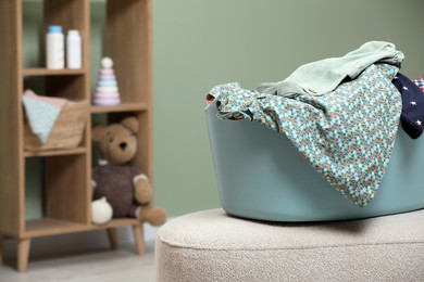 Photo of Laundry basket with baby clothes on light ottoman in child room, space for text