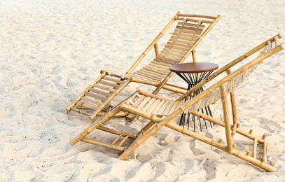 Empty wooden sunbeds and table on sandy shore. Beach accessories