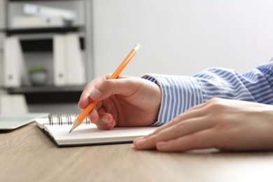 Woman writing in notebook at wooden table in office, closeup