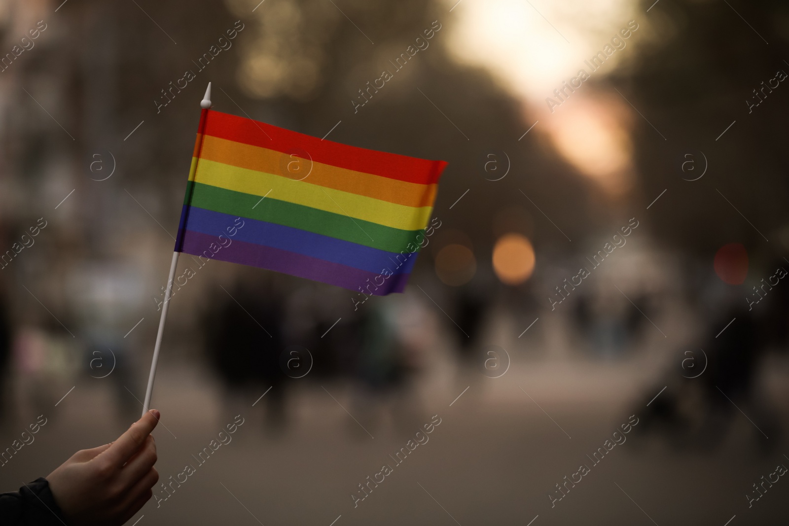 Photo of Woman holding small LGBT flag on city street, closeup. Space for text