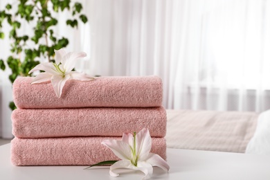 Photo of Stack of fresh towels with flowers on table in bedroom. Space for text