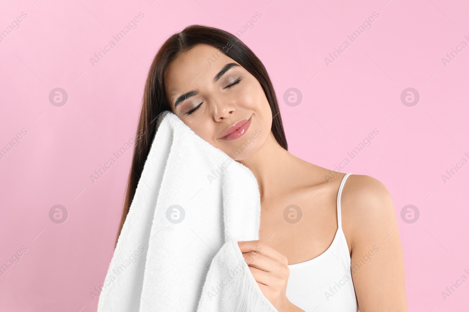 Photo of Young woman wiping face with towel on light pink background