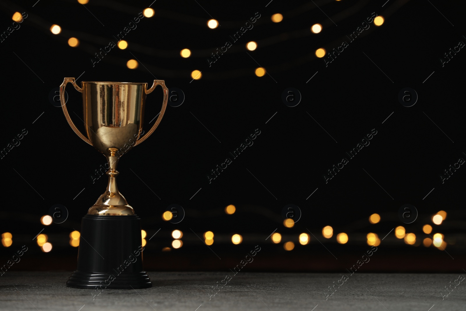 Photo of Golden trophy cup on table against blurred festive lights, space for text