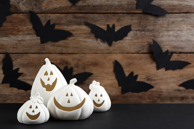 Image of White pumpkin shaped candle holders on black table against wooden wall with paper bats, space for text. Halloween decoration