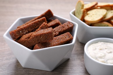 Photo of Different crispy rusks and dip sauce on wooden table, closeup