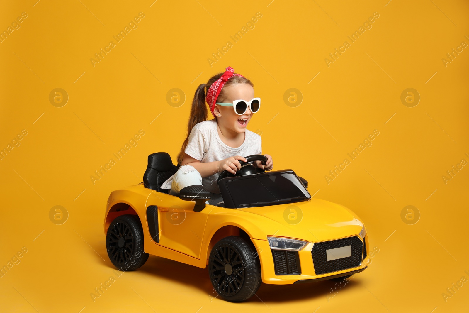 Photo of Cute little girl driving children's electric toy car on yellow background