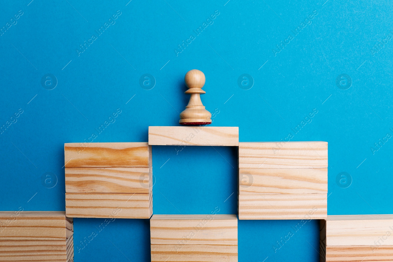 Photo of White pawn on bridge made of wooden blocks against light blue background, flat lay. Connection, relationships and deal concept