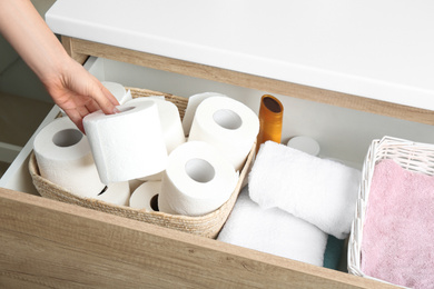Photo of Woman taking toilet paper roll from cabinet drawer, closeup