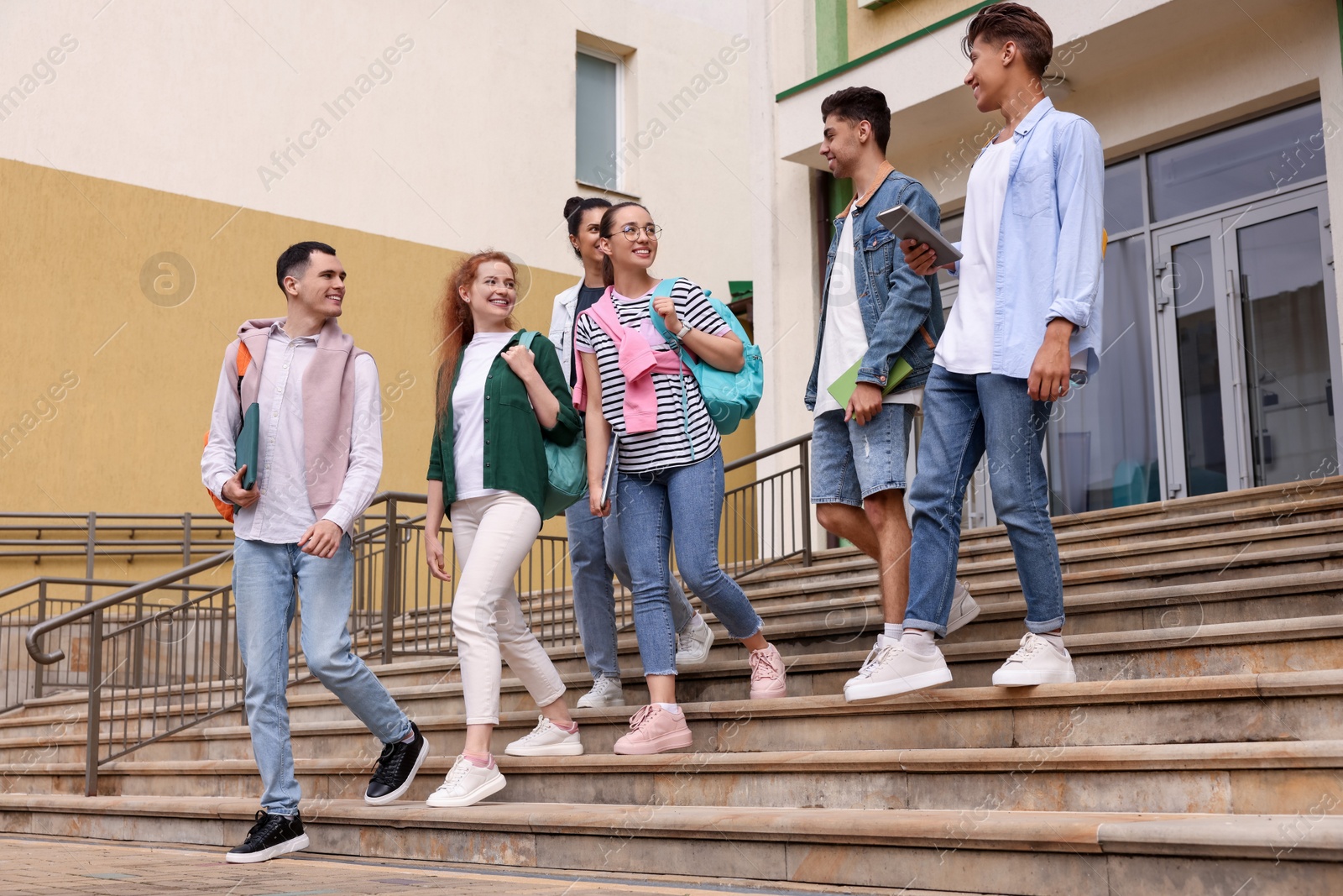Photo of Group of happy young students walking down stairs outdoors