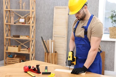 Photo of Young worker using electric drill at table in workshop