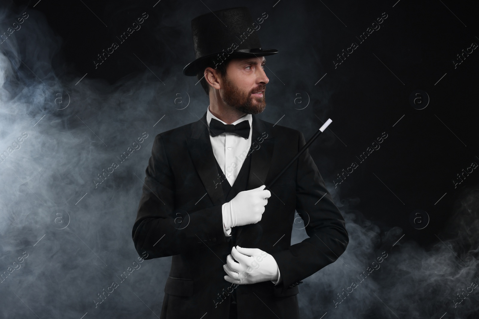 Photo of Magician holding wand in smoke on black background