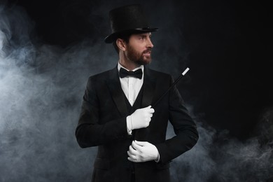 Photo of Magician holding wand in smoke on black background