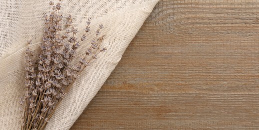 Beautiful dry lavender flowers and burlap fabric on wooden table, top view. Space for text