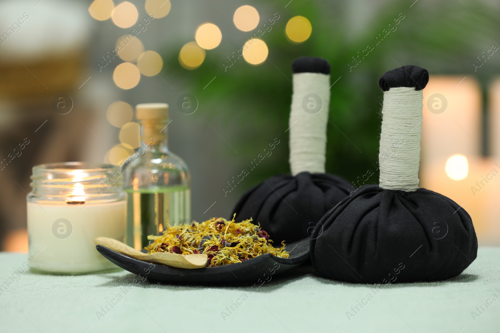 Photo of Spa composition. Herbal massage bags, essential oil and dry flowers on towel against blurred lights