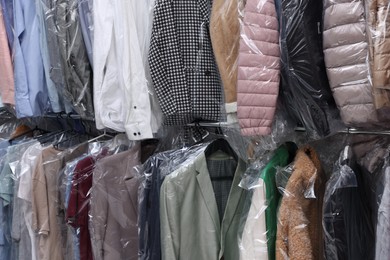Photo of Dry-cleaning service. Hangers with different clothes in plastic bags on rack