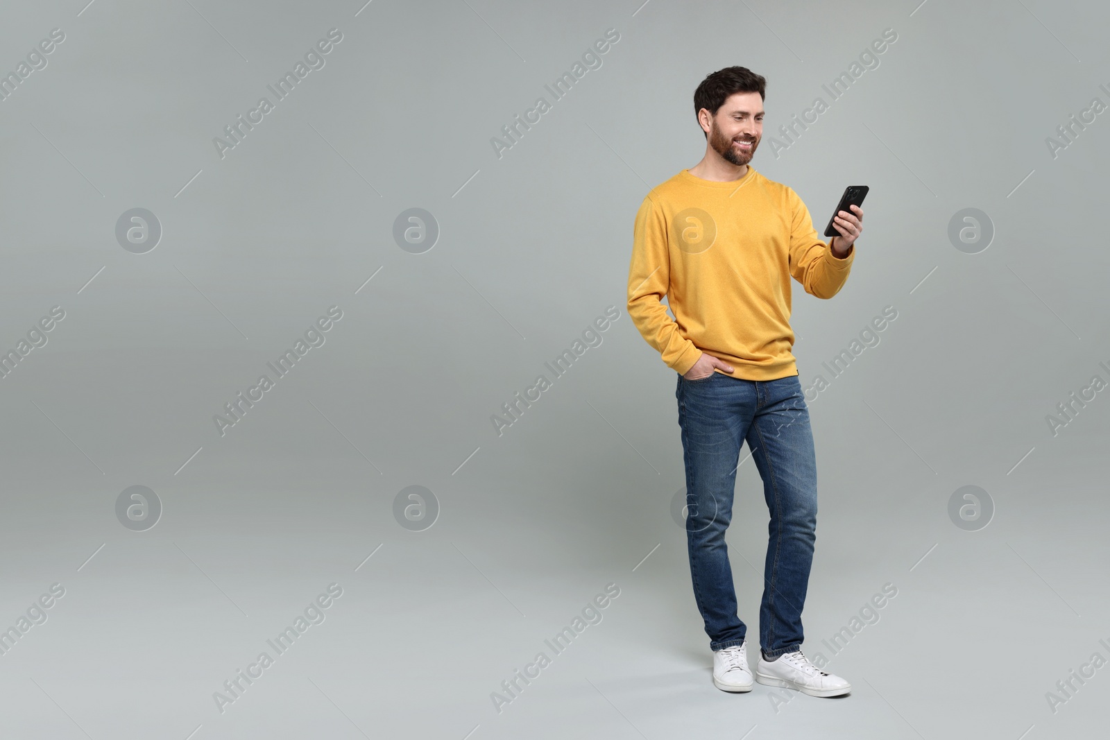 Photo of Smiling man with smartphone on grey background. Space for text