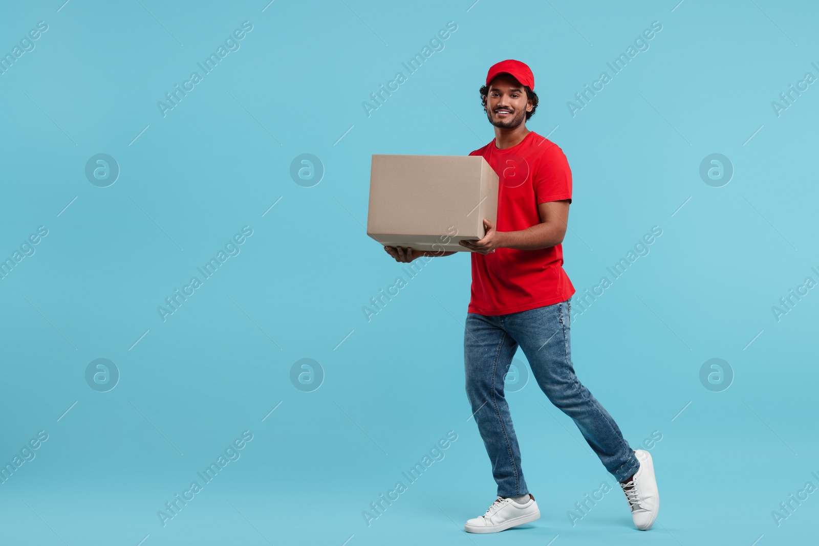 Photo of Happy young courier with parcel on light blue background, space for text