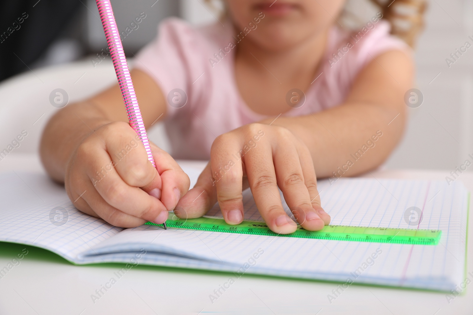 Photo of Little girl drawing with ruler and pencil at table, closeup. Doing homework