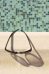 Photo of Stylish sunglasses near outdoor swimming pool on sunny day, top view