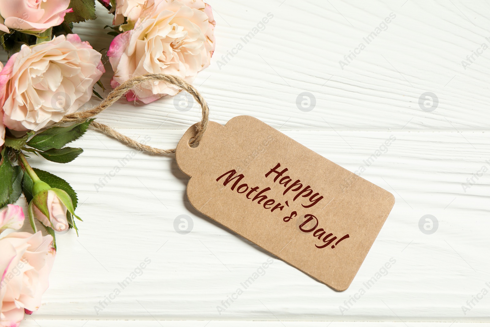 Image of Happy Mother's Day greeting label and beautiful rose flowers on white wooden table