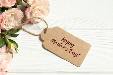 Happy Mother's Day greeting label and beautiful rose flowers on white wooden table