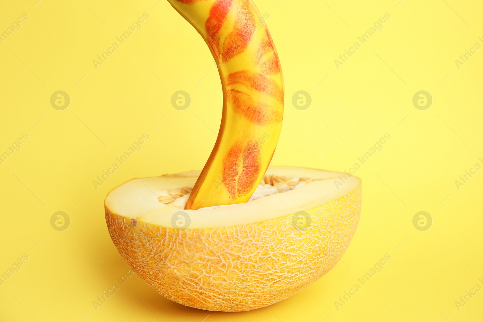 Photo of Fresh banana with red lipstick marks and melon on yellow background. Sex concept