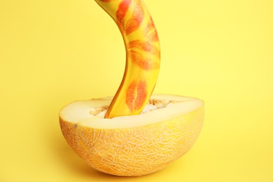 Fresh banana with red lipstick marks and melon on yellow background. Sex concept
