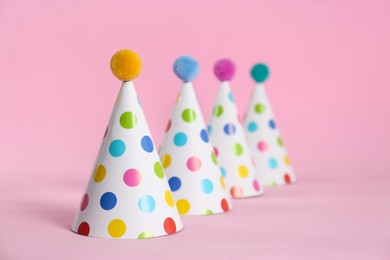 Colorful party hats with fluffy balls on pink background