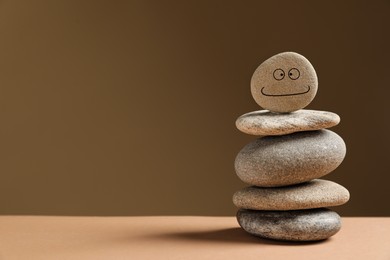 Photo of Stack of stones with drawn happy face on table against dark beige background, space for text. Zen concept