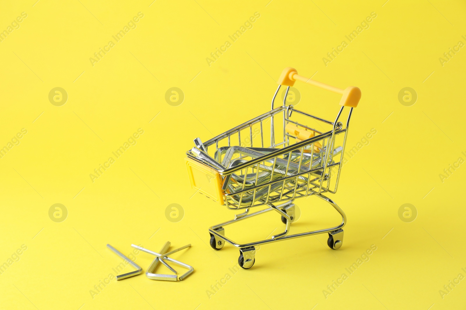 Photo of Small shopping cart with hexagon wrench set on yellow background. Construction tools