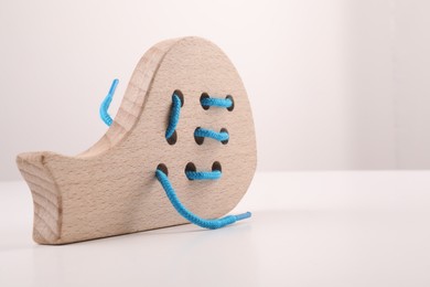 Photo of Motor skills development. Wooden lacing toy on white table, closeup. Space for text