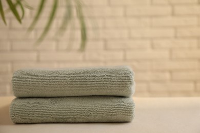 Photo of Stacked soft towels and green leaves on white table near brick wall indoors, space for text