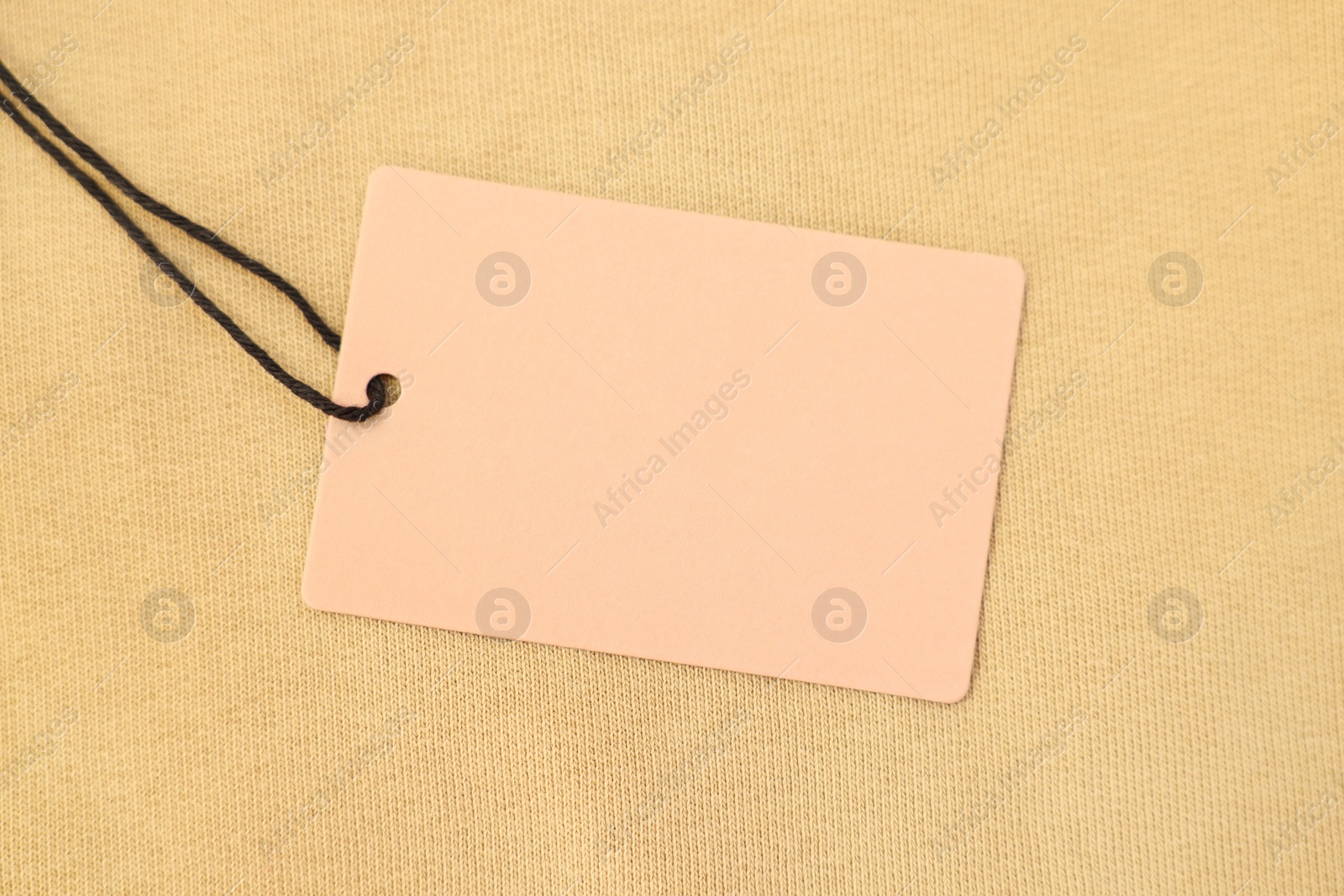 Photo of Cardboard tag on beige garment, top view. Space for text