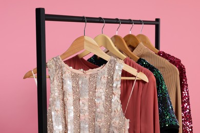Photo of Rack with stylish women's clothes on wooden hangers against pink background