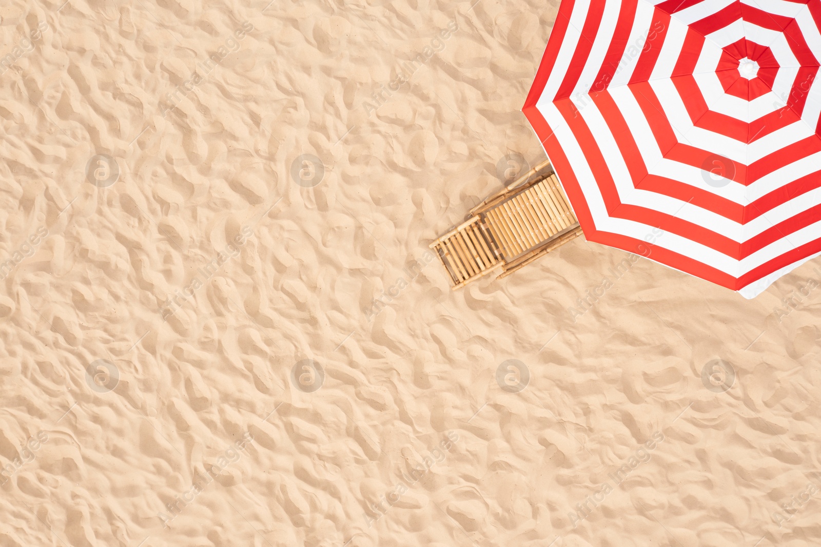 Image of Striped beach umbrella near wooden sunbed on sandy coast, aerial view. Space for text