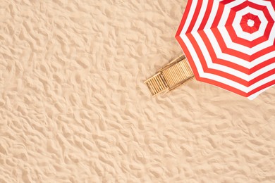 Image of Striped beach umbrella near wooden sunbed on sandy coast, aerial view. Space for text