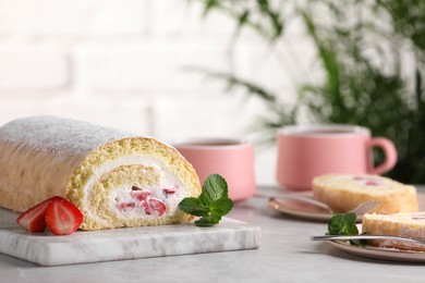 Photo of Delicious sponge cake roll with strawberries and cream on light grey table, space for text