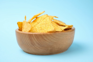 Wooden bowl with tasty Mexican nachos chips on light blue background