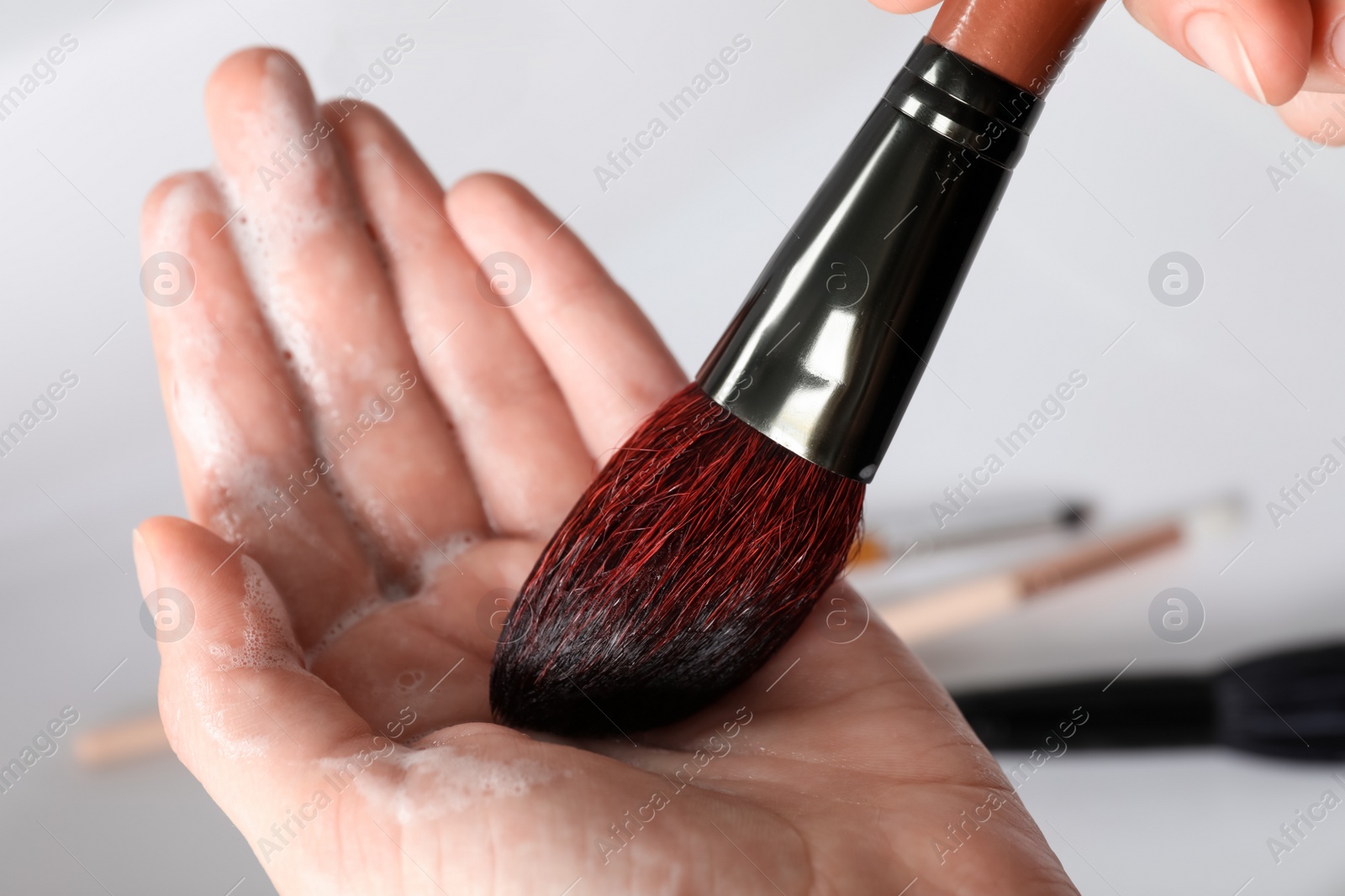 Photo of Woman washing makeup brush with soap, closeup