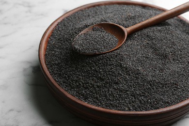 Poppy seeds and spoon in bowl on white marble table