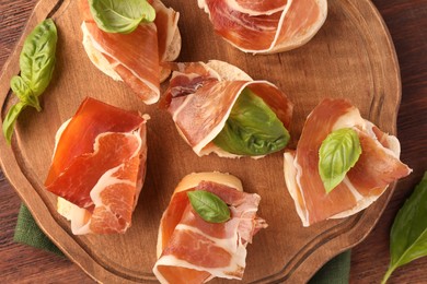 Board of tasty sandwiches with cured ham and basil leaves on wooden table, top view