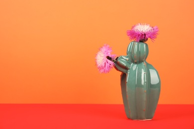 Trendy cactus shaped ceramic vase with flowers on table against color background