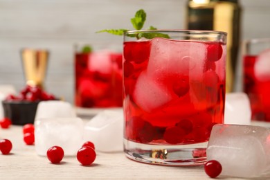 Photo of Tasty cranberry cocktail with ice cubes in glass and fresh berries on wooden table